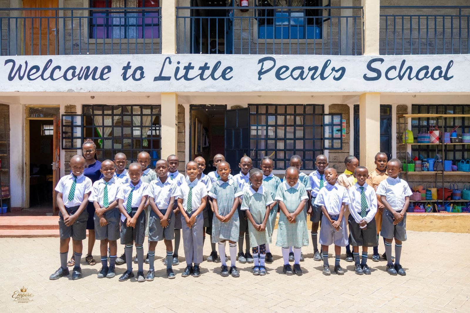 Little Pearls learners in uniform with their teacher in front of the 'Welcome to Little Pearls School' sign